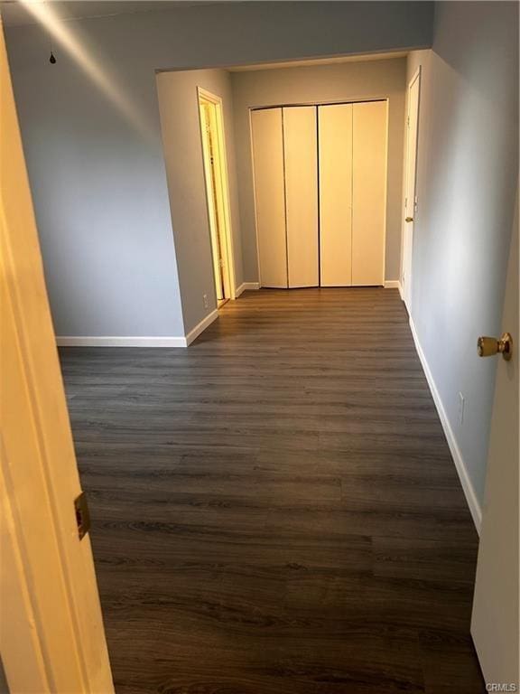 unfurnished bedroom with a closet, dark wood finished floors, and baseboards