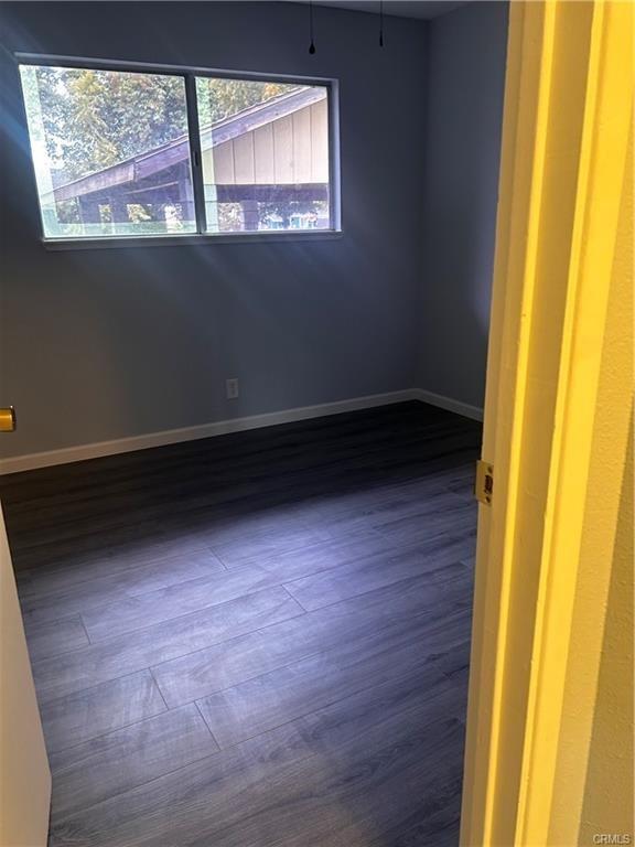 unfurnished room with dark wood-type flooring and baseboards