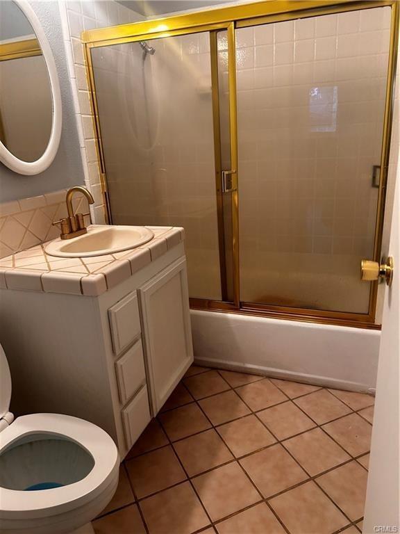 bathroom featuring bath / shower combo with glass door, vanity, toilet, and tile patterned floors