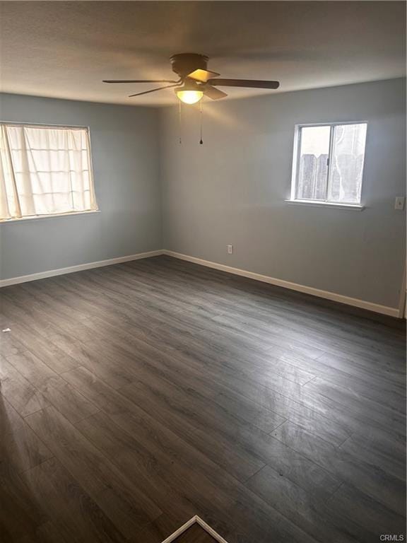 spare room featuring a healthy amount of sunlight, dark wood finished floors, and baseboards