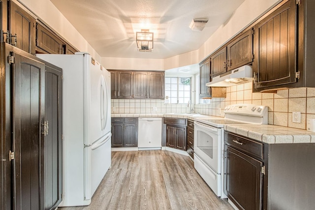 kitchen featuring tasteful backsplash, white appliances, light wood-type flooring, and under cabinet range hood