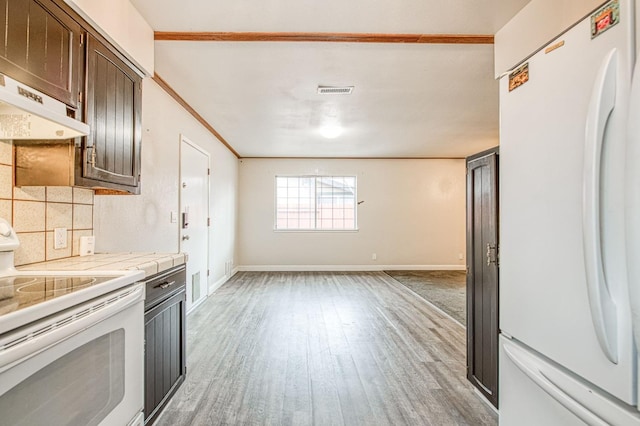 kitchen featuring under cabinet range hood, white appliances, light wood-style floors, dark brown cabinets, and tasteful backsplash