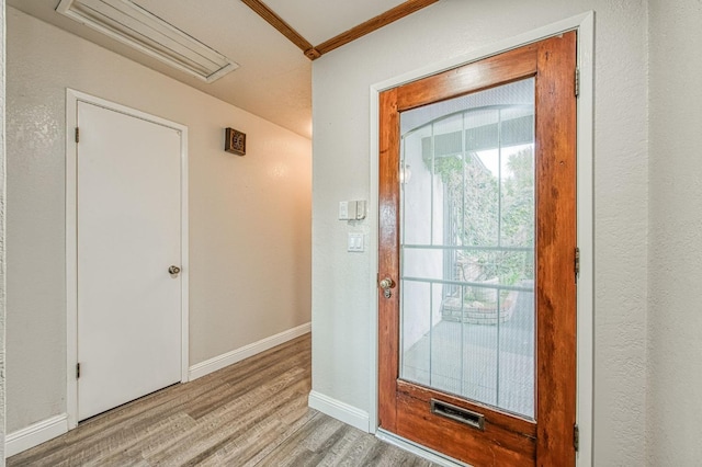 doorway with light wood-style flooring, visible vents, baseboards, and ornamental molding