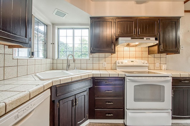 kitchen featuring under cabinet range hood, white appliances, a sink, dark brown cabinets, and tasteful backsplash