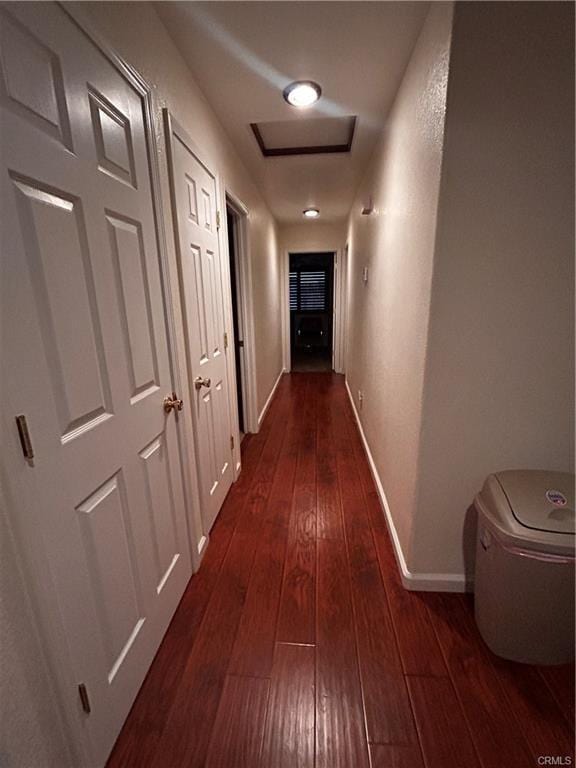 hall with attic access, baseboards, and dark wood-type flooring