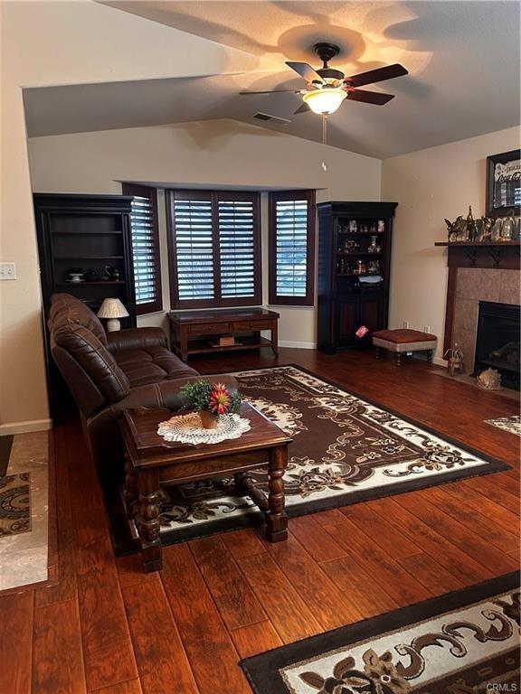 living area with lofted ceiling, visible vents, a ceiling fan, hardwood / wood-style floors, and a tiled fireplace