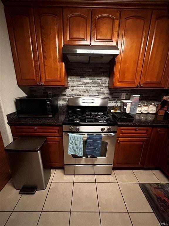 kitchen featuring stainless steel range with gas cooktop, light tile patterned floors, backsplash, black microwave, and under cabinet range hood