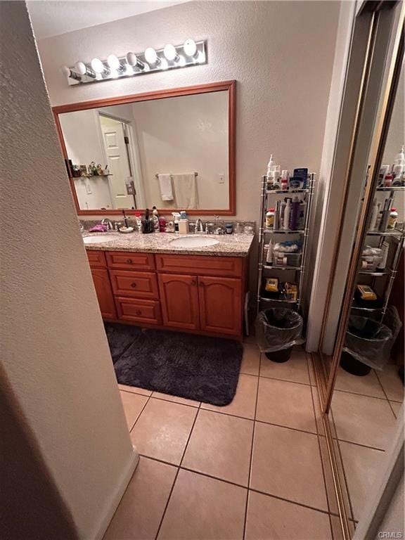 bathroom with double vanity, a textured wall, a sink, and tile patterned floors