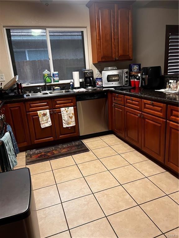 kitchen featuring appliances with stainless steel finishes, dark countertops, light tile patterned flooring, and a sink