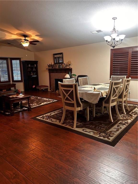 dining room with a fireplace, visible vents, a textured ceiling, hardwood / wood-style floors, and ceiling fan with notable chandelier