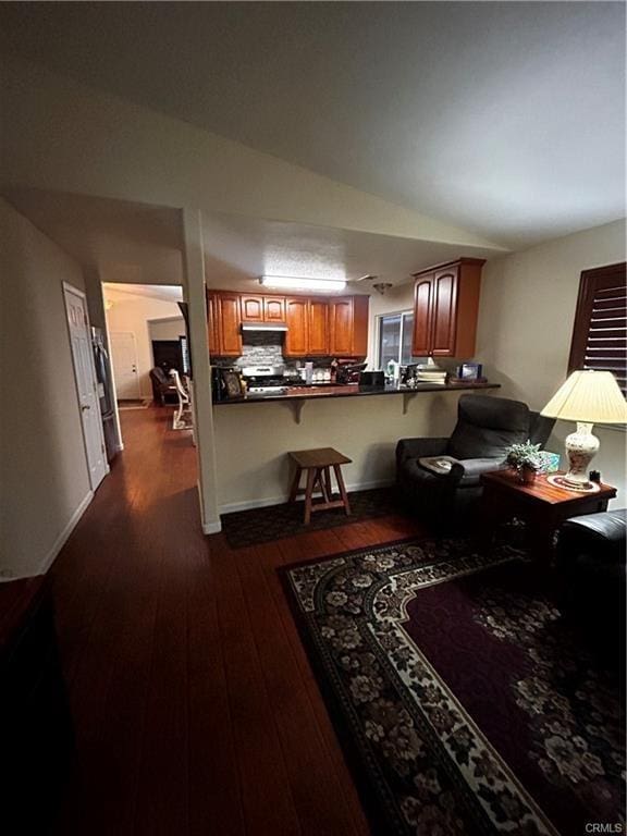 kitchen with brown cabinets, lofted ceiling, dark countertops, backsplash, and dark wood-type flooring