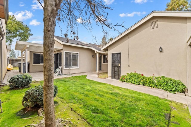 rear view of house featuring a yard, a patio, fence, and stucco siding