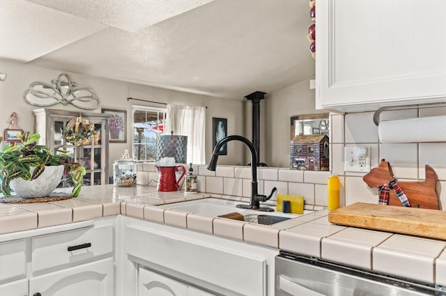 kitchen featuring a textured ceiling, a sink, white cabinets, stainless steel dishwasher, and decorative backsplash