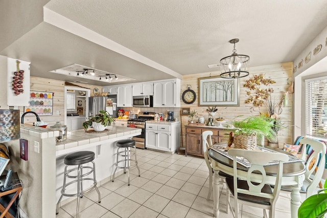 kitchen with tile countertops, a peninsula, wood walls, a kitchen breakfast bar, and appliances with stainless steel finishes