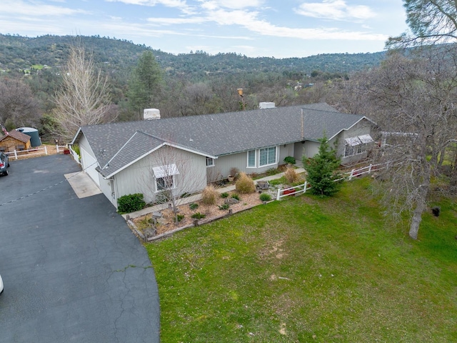 view of front facade with aphalt driveway, a front lawn, a shingled roof, and a forest view