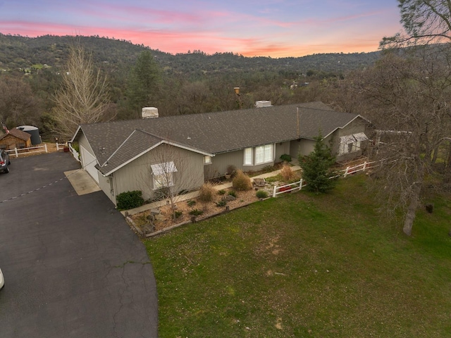 single story home featuring driveway, a forest view, and a lawn