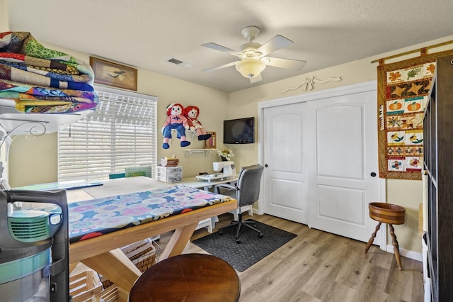 office area featuring light wood finished floors, visible vents, a ceiling fan, a textured ceiling, and baseboards