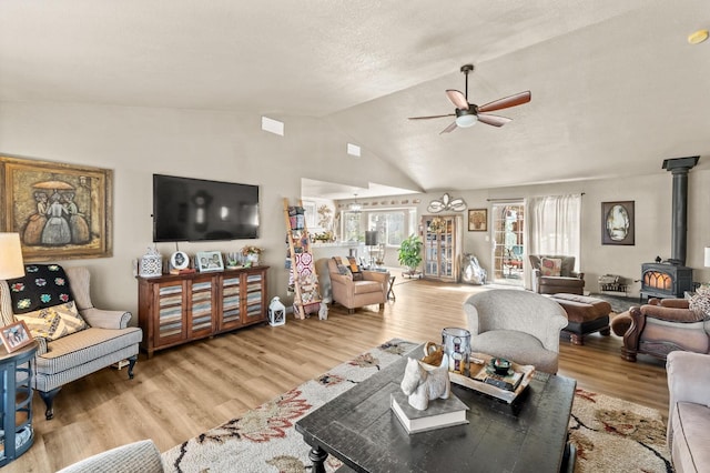 living area featuring a wood stove, light wood-style floors, vaulted ceiling, and a ceiling fan