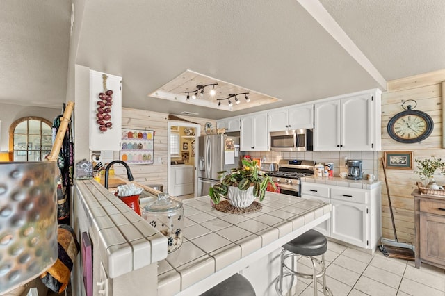 kitchen featuring tile countertops, light tile patterned floors, appliances with stainless steel finishes, wooden walls, and a textured ceiling