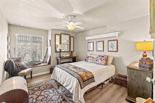 bedroom with baseboards, visible vents, a ceiling fan, wood finished floors, and a textured ceiling