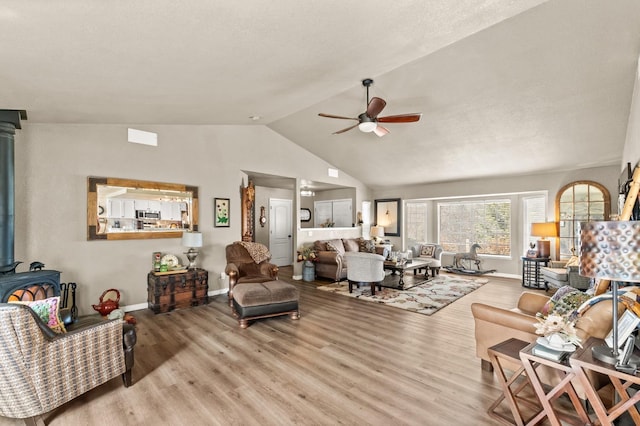 living area featuring lofted ceiling, wood finished floors, a wood stove, and a ceiling fan