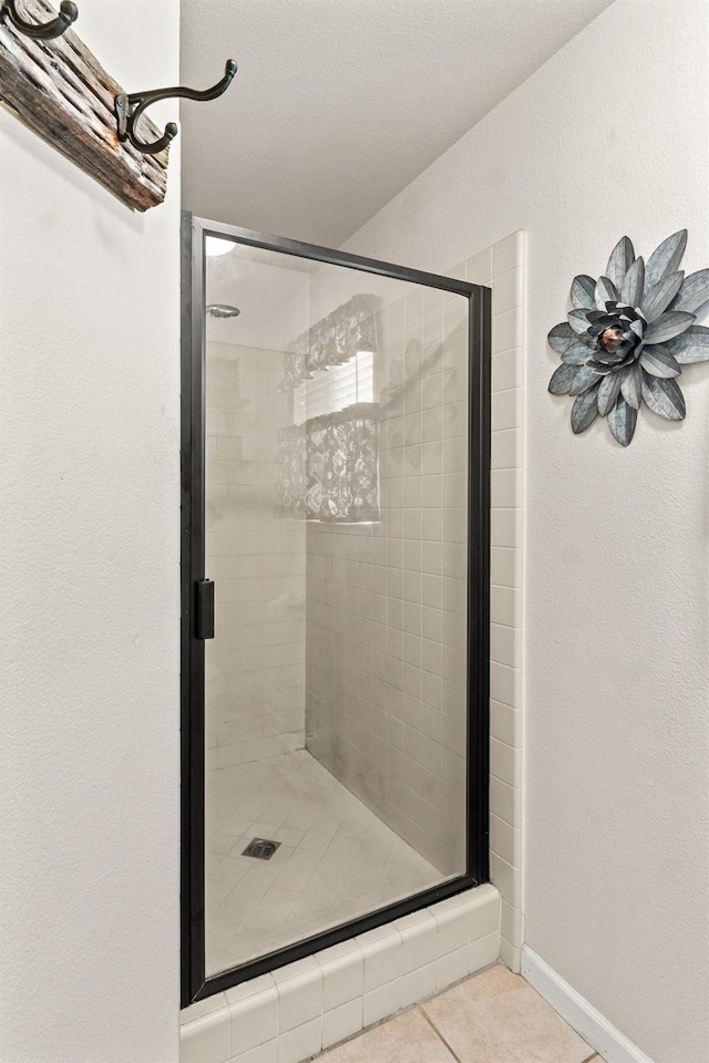 bathroom with baseboards, a textured wall, a stall shower, and tile patterned floors