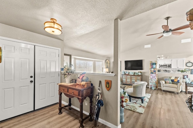 foyer featuring lofted ceiling, a textured ceiling, light wood-type flooring, and baseboards