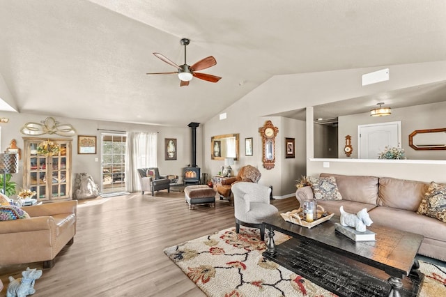 living room with a wood stove, ceiling fan, vaulted ceiling, and wood finished floors