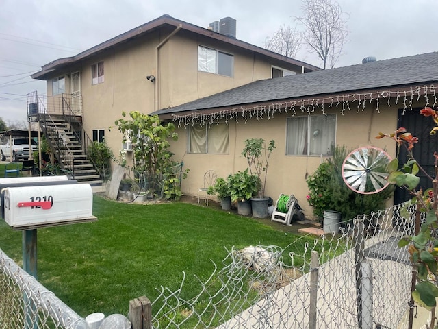 exterior space featuring a shingled roof, a lawn, stairway, fence, and stucco siding