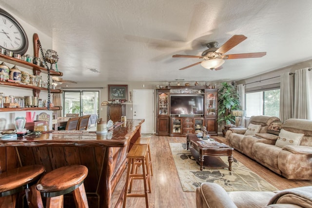 bar featuring a textured ceiling, a healthy amount of sunlight, ceiling fan, and light wood finished floors