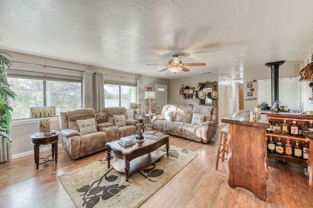 living room featuring baseboards, ceiling fan, a wood stove, light wood-style floors, and a textured ceiling