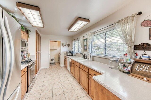 kitchen with light countertops, light tile patterned floors, appliances with stainless steel finishes, washer / clothes dryer, and a sink