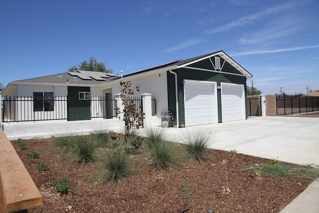 view of front facade with stucco siding, solar panels, an attached garage, fence private yard, and driveway