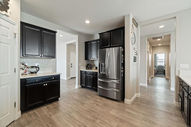 kitchen with dark cabinets, visible vents, light countertops, light wood-type flooring, and stainless steel fridge with ice dispenser