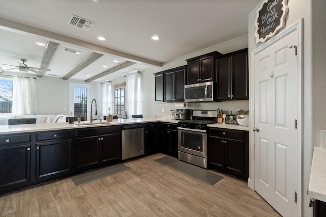 kitchen featuring visible vents, appliances with stainless steel finishes, beamed ceiling, light wood-type flooring, and a sink