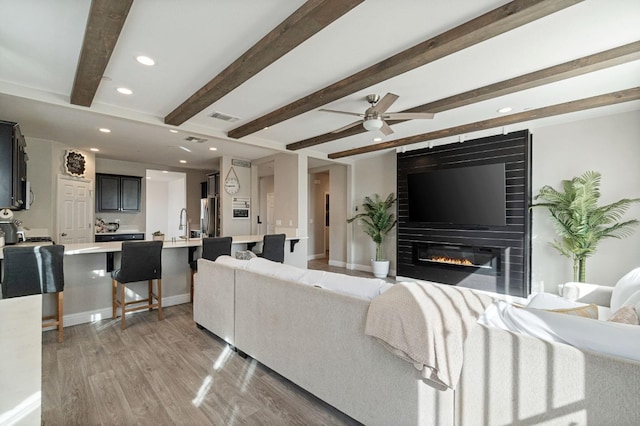 living area with a fireplace, light wood finished floors, recessed lighting, visible vents, and beamed ceiling