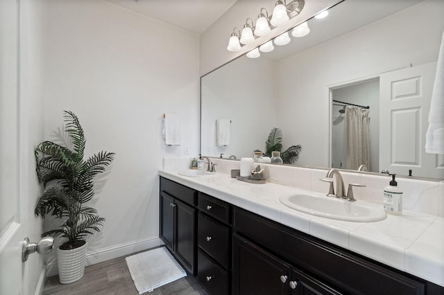 full bathroom with double vanity, a sink, baseboards, and wood finished floors