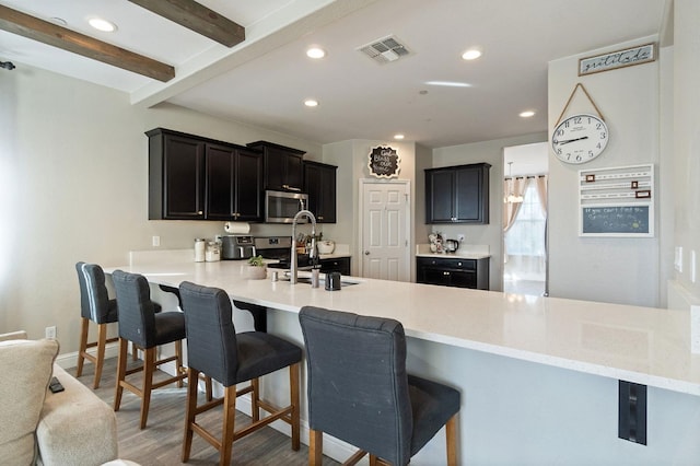 kitchen with beam ceiling, visible vents, stainless steel microwave, a sink, and a peninsula