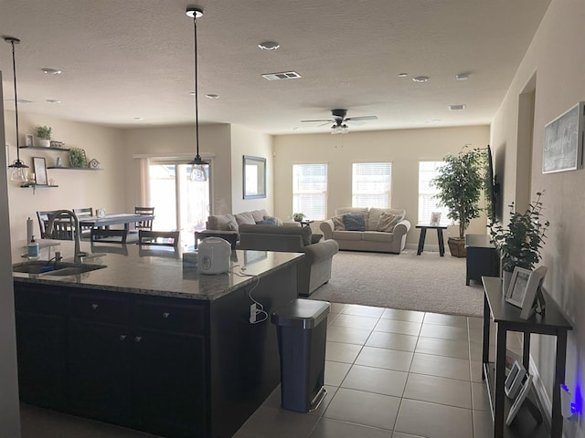 kitchen featuring a textured ceiling, a sink, visible vents, dark cabinetry, and tile patterned floors