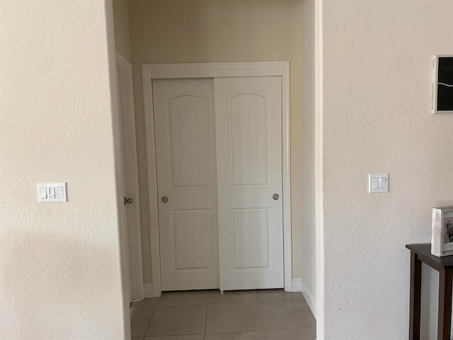 hallway featuring light tile patterned floors, a textured wall, and baseboards