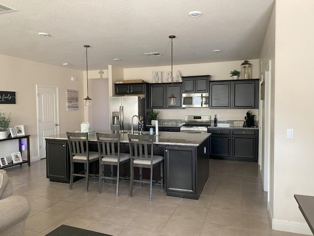 kitchen featuring visible vents, stainless steel appliances, a kitchen bar, and a kitchen island with sink