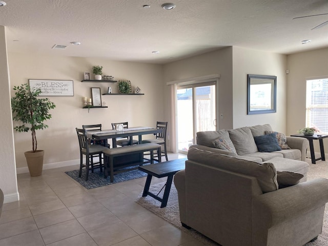 living area with tile patterned flooring, plenty of natural light, a textured ceiling, and baseboards