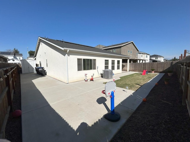 back of property featuring an outbuilding, central air condition unit, a patio area, a shed, and stucco siding