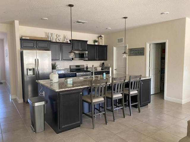 kitchen with light stone counters, appliances with stainless steel finishes, a kitchen bar, and a large island with sink