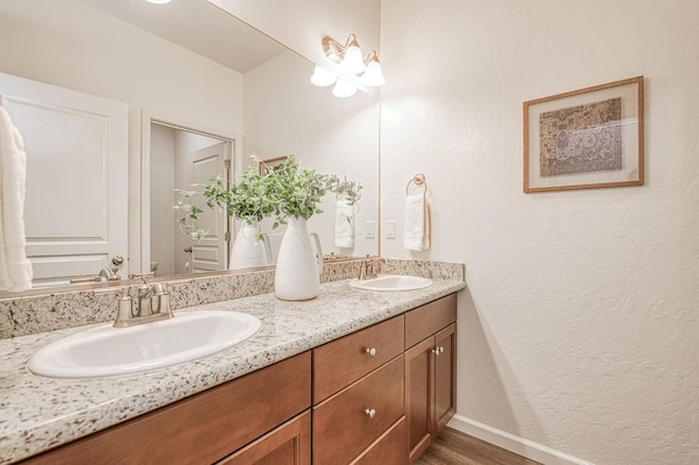 bathroom with wood finished floors, a sink, baseboards, and double vanity