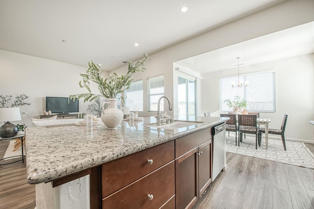 kitchen featuring light stone counters, a kitchen island with sink, wood finished floors, a sink, and dishwasher