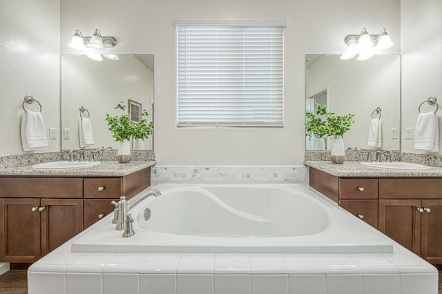 bathroom featuring a bath, two vanities, and a sink