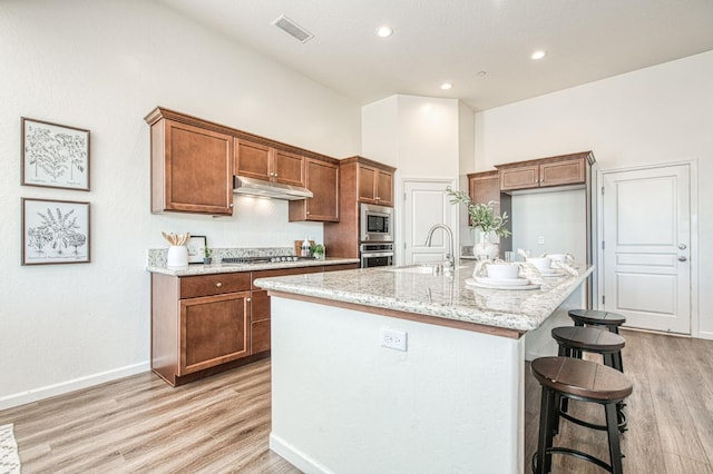 kitchen featuring under cabinet range hood, a sink, visible vents, appliances with stainless steel finishes, and brown cabinets