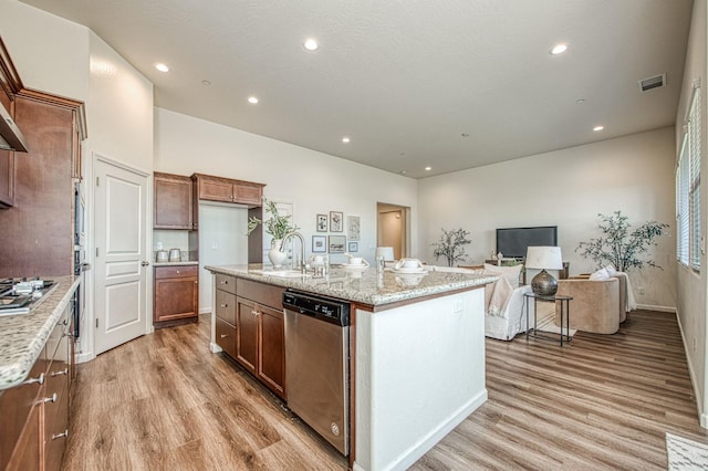 kitchen with appliances with stainless steel finishes, a sink, light stone counters, and light wood-style floors