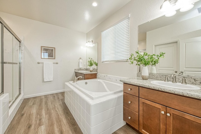 full bathroom with a garden tub, two vanities, a stall shower, a sink, and wood finished floors